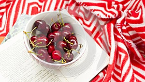 The book and red ripe cherries. Two ripe cherries look out of the book. Cherries as an unusual bookmark for the book. Notebook for
