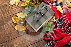 Book, red scarf, pencil, glasses and fallen leaves on wooden table. Autumn mood, poetry, education or back to school concept