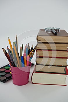 Book stack, magnifying glass, color pencils and palette on white background