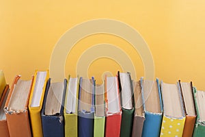 Book stacking. Open hardback books on wooden table and yellow background. Back to school. Copy space for ad text