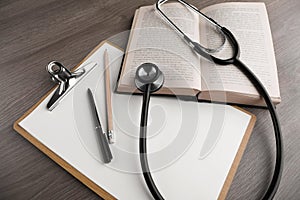 Book, stethoscope and stationery on wooden table, above view. Medical education