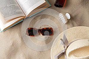 book, sunglasses and sunscreen on beach sand