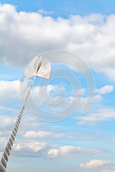 Book tied on cord soars into light blue sky