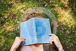 This book is too much. an unrecognizable woman reading a book while lying outside on the grass.