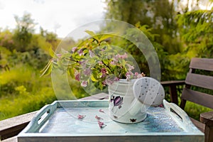 Book on the white vintage table with vase and sunglasses on green grass on sunny summer day, soft focus. Lawn with spring flowers