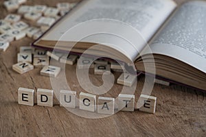 Book and the word educate written with cube letters on wood