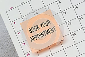 Book your appointment text on sticky note and stuck to a calendar background.