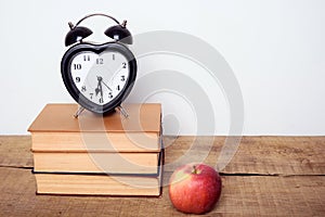 Books, alarm clock and apple on wooden background