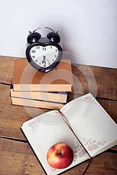 Books, alarm clock, notepad and apple on wooden background