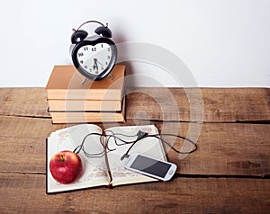 Books, alarm clock, notepad, cellphone and apple on wooden background