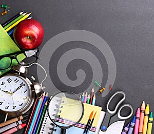 Books, apple, alarm clock and pencils on black board