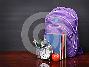 Books, apple, backpack, alarm clock and pencils on wood desk
