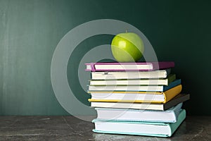 Books and apple on grey table near chalkboard. School education
