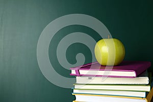 Books and apple near green chalkboard. School education