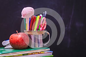Books, apple, pens and pencils on wooden table, against the background of a chalk board. Concept for Teacher`s Day, copy space
