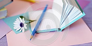 Books with bookmarks of flowers, pencils, notepads on the table, on a background of colored paper