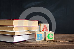 Books and cubes with the letters ABC on wooden table against the background of the chalkboard.