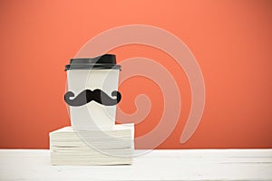 Books and cup with mustache on wooden table