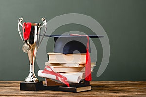 Books, diploma, academic cap, trophy cup and medal on wooden surface