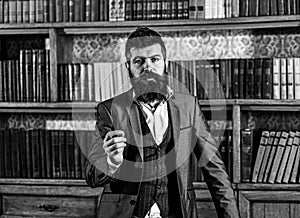 Books and literature. Speaker with calm face stands in vintage interior. Bearded man in elegant suit near bookcase