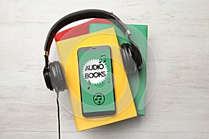 Books with modern headphones and smartphone on wooden background, top view