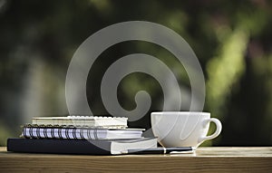 The books and notebook with coffee mug and a pen put on wooden in nature park in the morning atmosphere