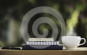 The books and notebook with coffee mug and a pen put on wooden in nature park in the morning atmosphere