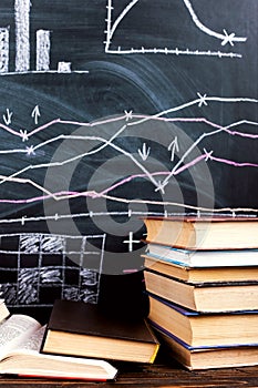 Books on the table against the background of a chalkboard on which are drawn graphs and charts of growth and decline. Business