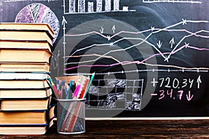 Books on the table against the background of a chalkboard on which are drawn graphs and charts of growth and decline. Business