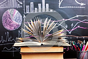 Books on the table against the background of a chalkboard on which are drawn graphs and charts of growth and decline. Business