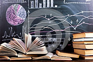 Books on the table against the background of a chalkboard on which are drawn graphs and charts of growth and decline. Business