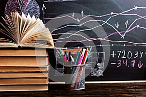 Books on the table against the background of a chalkboard on which are drawn graphs and charts of growth and decline. Business