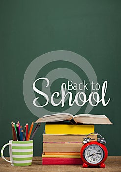 Books on the table against green blackboard with back to school text