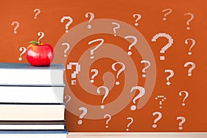 Books on the table against orange blackboard with question marks