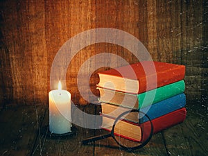 Books and a white candle on a wooden table. Reading by candlelight. Vintage composition.