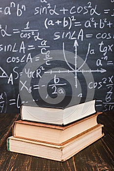 Books on a wooden table, against the background of a chalk board with formulas. Teacher's day concept and back to school