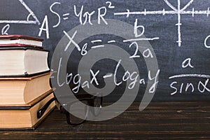 Books on a wooden table, against the background of a chalk board with formulas. Teacher's day concept and back to school