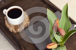 Books on a wooden table. A cup of coffee. Flowers on the book. A stack of books. Workplace.