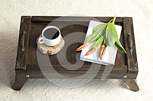 Books on a wooden tray. A cup of coffee. Flowers on the book. A stack of books. Workplace.