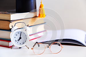 Books, writing materials, glasses, notebook and alarm clock on the desktop