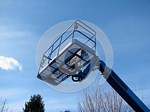 Boom lift reaching high up. Blue elevated work bucket platform.