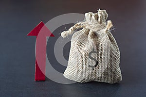 Boost or increase your income with directional arrow, money and a bag over dark background. Financial concept. Copy space