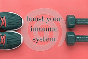 Boost your immune system - lettering on banner, sport concept. Purple running shoes and two dumbbells on pink background