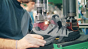 A boot is getting put together with its sole by a male worker. Shoes production factory.