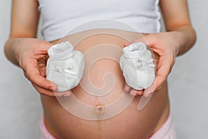 Booties for newborn in the hands of a pregnant girl on the background of the abdomen