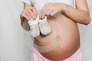 Booties for newborn in the hands of a pregnant girl on the background of the abdomen