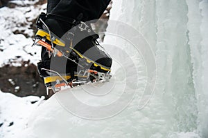 Boots and crampons of an ice climber on a frozen waterfall