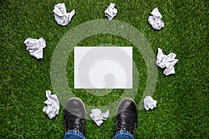 Boots and sheet of paper with cramled sheets on the grass