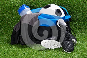 Boots, soccer ball, T-shirt and a water bottle, in a sports bag, against the background of grass