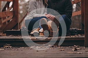 Boots of young couple walking outdoor on wooden bridge in autumn